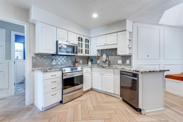 kitchen with appliances with stainless steel finishes, light parquet flooring, white cabinetry, decorative backsplash, and light stone counters