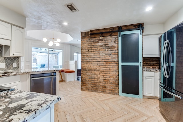 kitchen with white cabinetry, decorative backsplash, black fridge, light stone counters, and light parquet floors