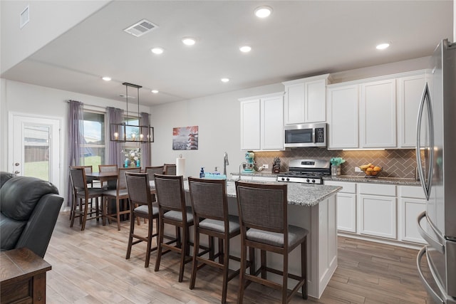 kitchen featuring stainless steel appliances, pendant lighting, white cabinets, and an island with sink