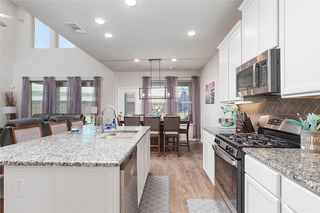 kitchen with white cabinets, appliances with stainless steel finishes, decorative backsplash, sink, and a center island with sink