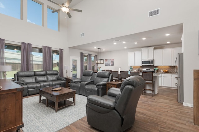 living room with ceiling fan, a towering ceiling, and hardwood / wood-style floors