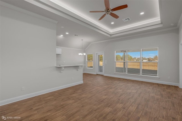 unfurnished living room with ceiling fan with notable chandelier, a tray ceiling, crown molding, and a healthy amount of sunlight