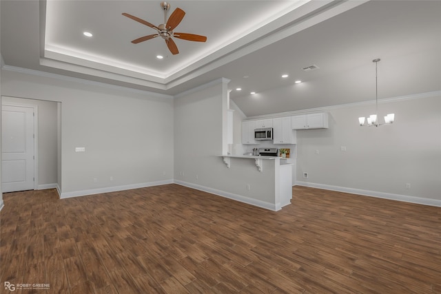 unfurnished living room with dark wood-type flooring, ornamental molding, ceiling fan with notable chandelier, and a tray ceiling