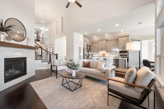 living room featuring ceiling fan with notable chandelier, a towering ceiling, light hardwood / wood-style floors, sink, and a tile fireplace