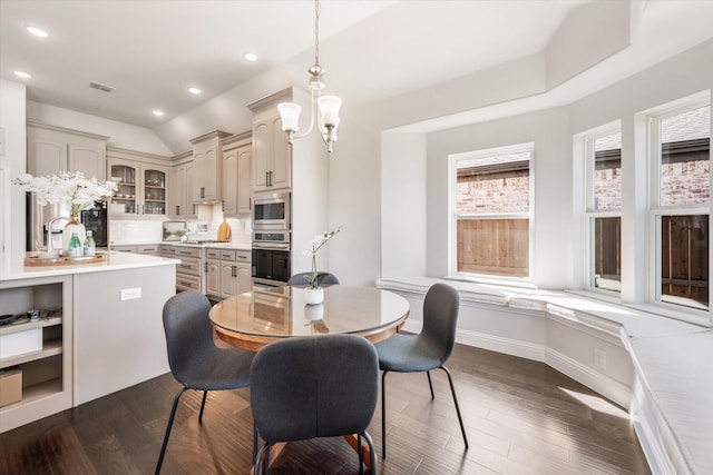 dining area featuring vaulted ceiling, dark wood-type flooring, sink, and a notable chandelier