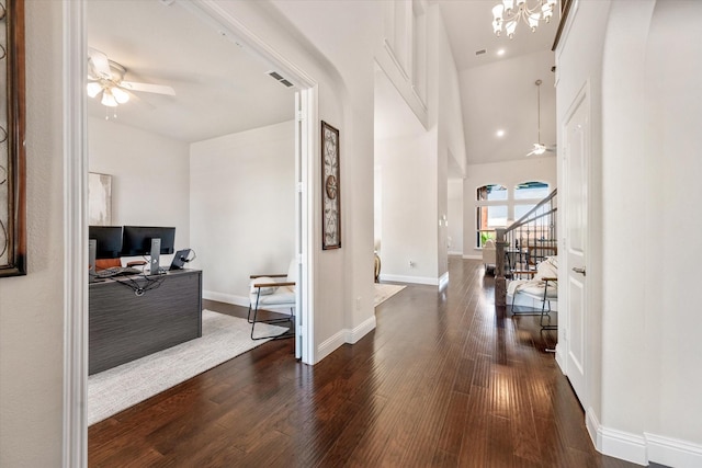 hall with dark hardwood / wood-style flooring, a towering ceiling, and a notable chandelier