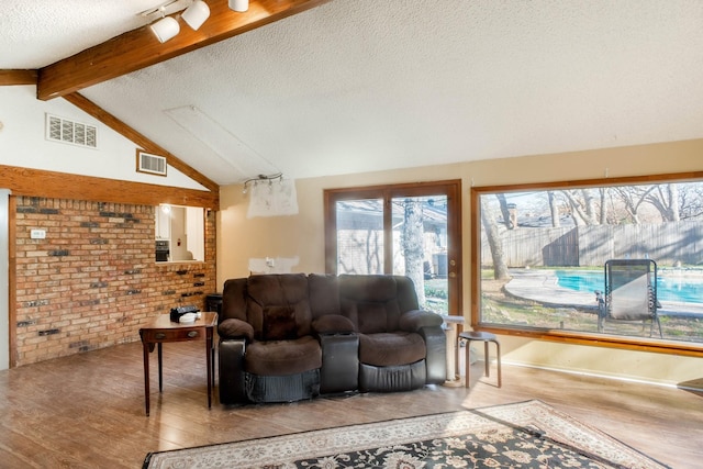 living room featuring a textured ceiling, brick wall, hardwood / wood-style flooring, and lofted ceiling with beams