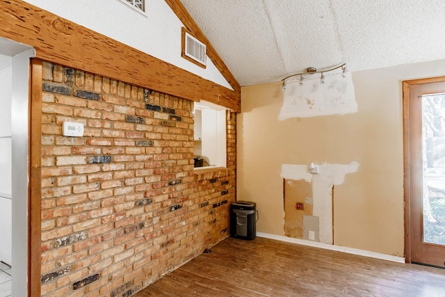 interior space featuring vaulted ceiling, brick wall, a textured ceiling, and wood-type flooring