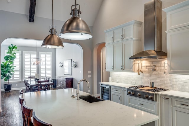 kitchen with white cabinets, sink, stainless steel gas cooktop, and wall chimney range hood