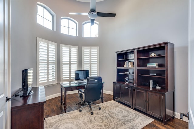 home office featuring ceiling fan, dark wood-type flooring, and a towering ceiling