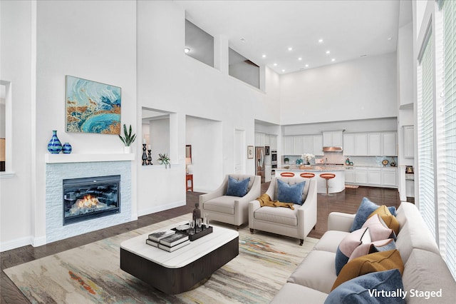 living room featuring a stone fireplace, a towering ceiling, and dark wood-type flooring