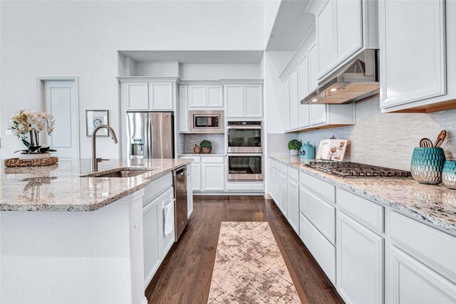 kitchen with a sink, decorative backsplash, white cabinets, under cabinet range hood, and appliances with stainless steel finishes