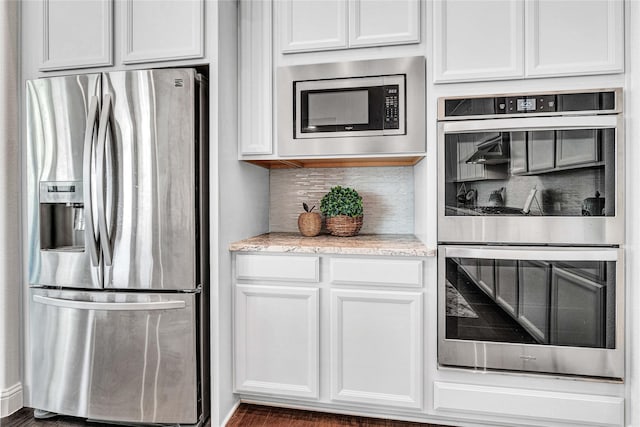 kitchen featuring appliances with stainless steel finishes, white cabinets, backsplash, and light stone counters