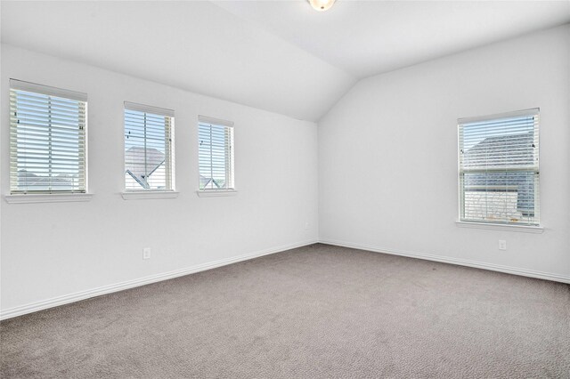 carpeted empty room featuring a wealth of natural light, baseboards, and lofted ceiling