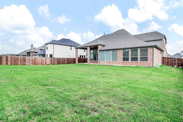 back of house with brick siding, a yard, a fenced backyard, and roof with shingles