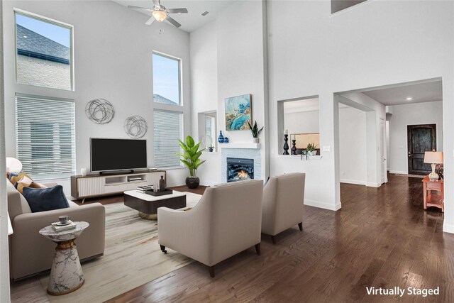 living room with baseboards, a fireplace, a towering ceiling, wood finished floors, and a ceiling fan