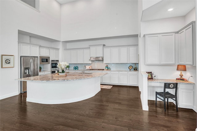 kitchen with a sink, light stone counters, a high ceiling, stainless steel appliances, and dark wood-style flooring