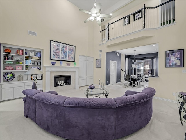 carpeted living room with a towering ceiling, ceiling fan, and a premium fireplace