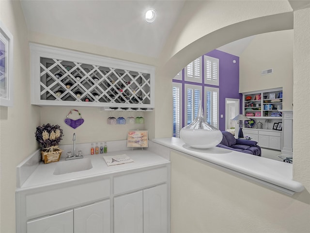 bar with lofted ceiling, white cabinets, and sink