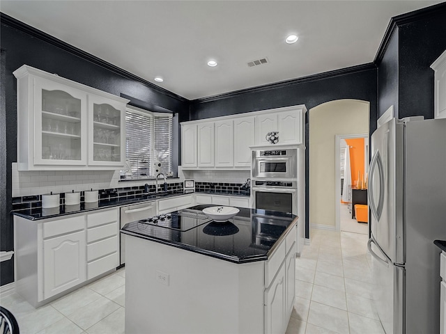 kitchen with white cabinets, a kitchen island, stainless steel appliances, backsplash, and ornamental molding