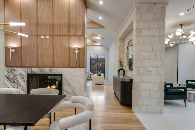 living room featuring a stone fireplace, light wood-type flooring, high vaulted ceiling, a chandelier, and beamed ceiling