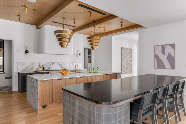 kitchen featuring wooden ceiling, hanging light fixtures, a large island with sink, light hardwood / wood-style flooring, and beamed ceiling