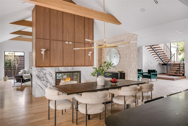 dining room featuring high vaulted ceiling, a chandelier, light hardwood / wood-style flooring, and beamed ceiling