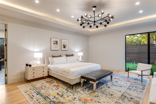 bedroom featuring a raised ceiling, access to exterior, a notable chandelier, and light hardwood / wood-style flooring