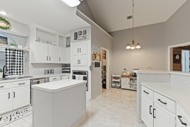 kitchen featuring stainless steel oven, decorative light fixtures, a kitchen island, white cabinets, and sink