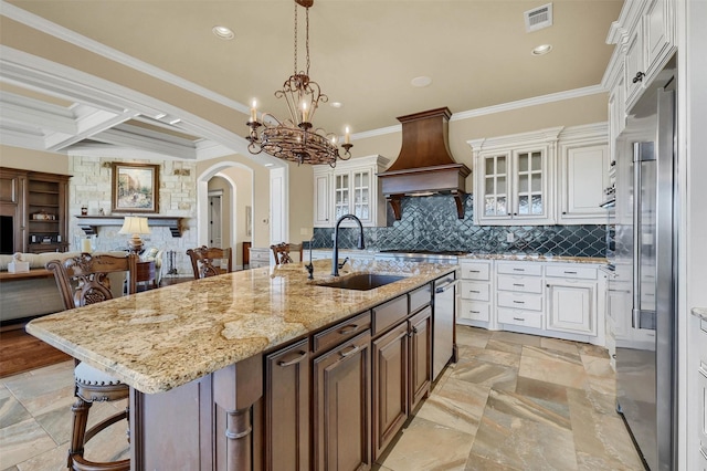 kitchen with appliances with stainless steel finishes, white cabinetry, sink, a kitchen island with sink, and custom range hood