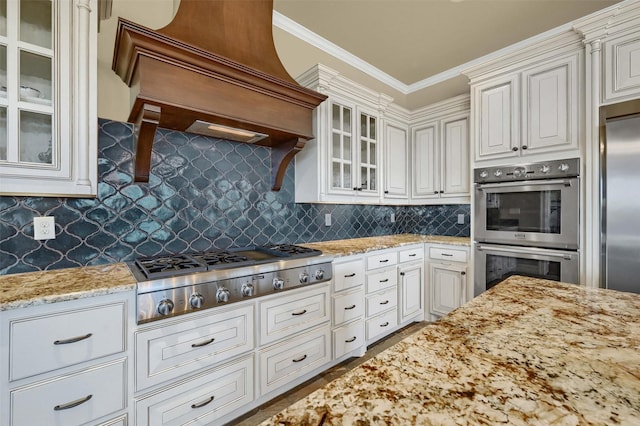 kitchen featuring custom exhaust hood, appliances with stainless steel finishes, backsplash, crown molding, and white cabinets