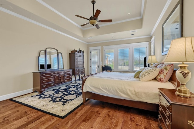 bedroom with dark wood-type flooring, ceiling fan, ornamental molding, and a raised ceiling