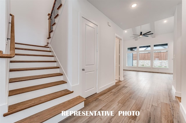 stairs with ceiling fan, hardwood / wood-style floors, and lofted ceiling