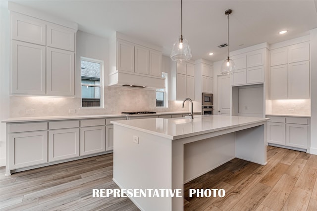 kitchen with decorative light fixtures, white cabinets, appliances with stainless steel finishes, and a center island with sink