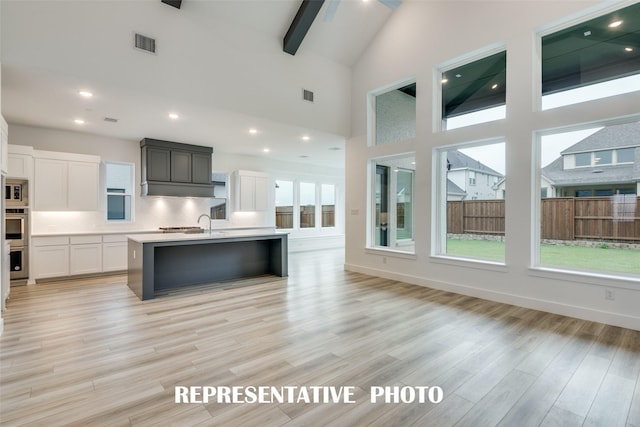 kitchen featuring white cabinets, light wood-type flooring, beam ceiling, and an island with sink