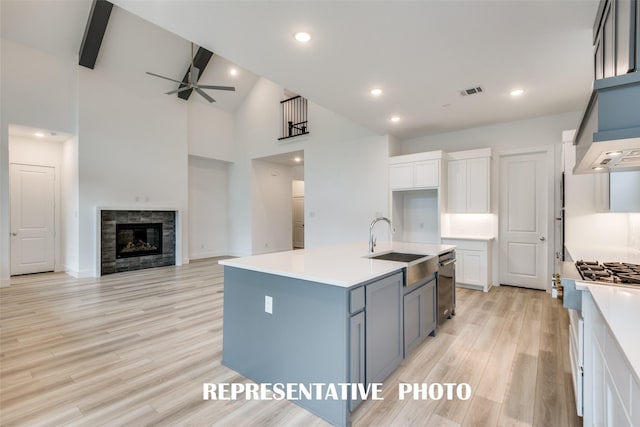 kitchen featuring white cabinets, a fireplace, light wood-type flooring, ceiling fan, and a center island with sink