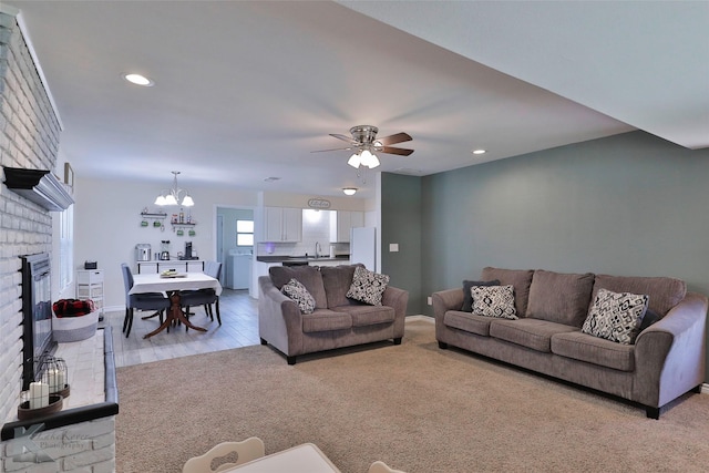 living room with a brick fireplace, light colored carpet, washer / dryer, and ceiling fan with notable chandelier