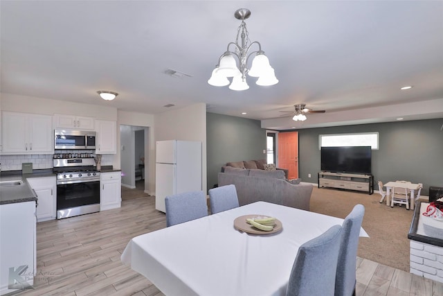 dining area featuring ceiling fan with notable chandelier, light hardwood / wood-style flooring, and sink