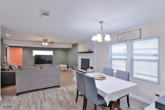 dining space featuring a brick fireplace, ceiling fan with notable chandelier, and light hardwood / wood-style flooring