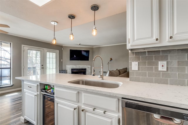 kitchen with decorative light fixtures, stainless steel dishwasher, sink, light stone countertops, and white cabinets