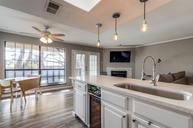 kitchen featuring wine cooler, hanging light fixtures, light stone countertops, white cabinets, and sink