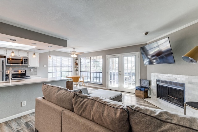 living room with ceiling fan, light wood-type flooring, french doors, a tile fireplace, and sink