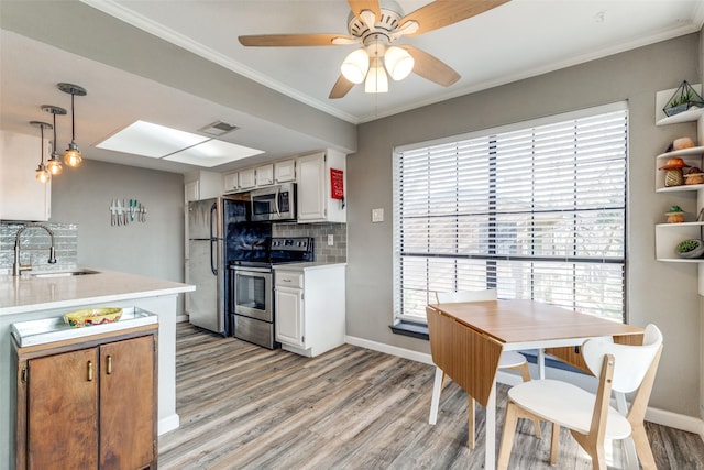 kitchen with stainless steel appliances, backsplash, decorative light fixtures, white cabinets, and sink