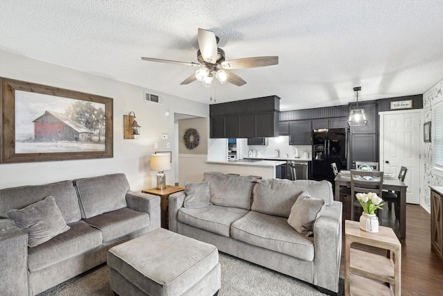 living room with a textured ceiling, ceiling fan, hardwood / wood-style flooring, and sink