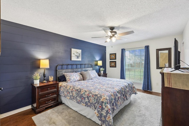 bedroom featuring ceiling fan, dark hardwood / wood-style floors, wooden walls, and a textured ceiling