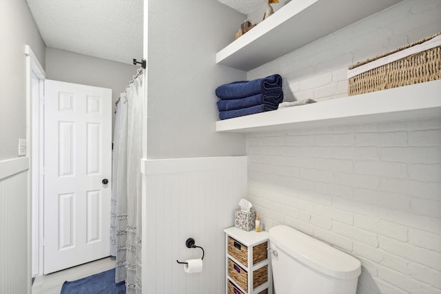 bathroom with brick wall, a textured ceiling, and toilet