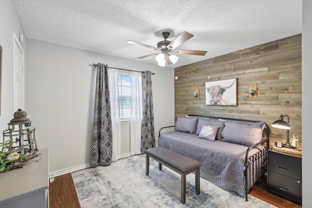 bedroom featuring a textured ceiling, ceiling fan, hardwood / wood-style floors, and wooden walls