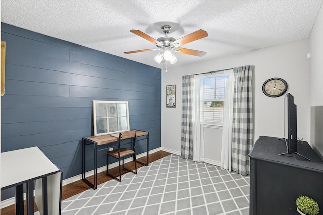 interior space with ceiling fan, a textured ceiling, and wood walls