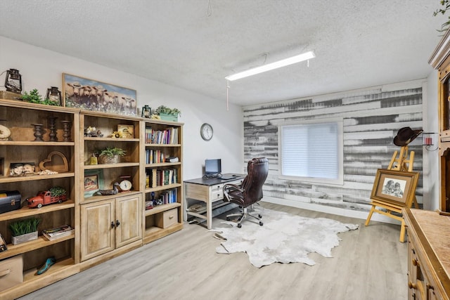 home office with a textured ceiling, light hardwood / wood-style flooring, and wooden walls