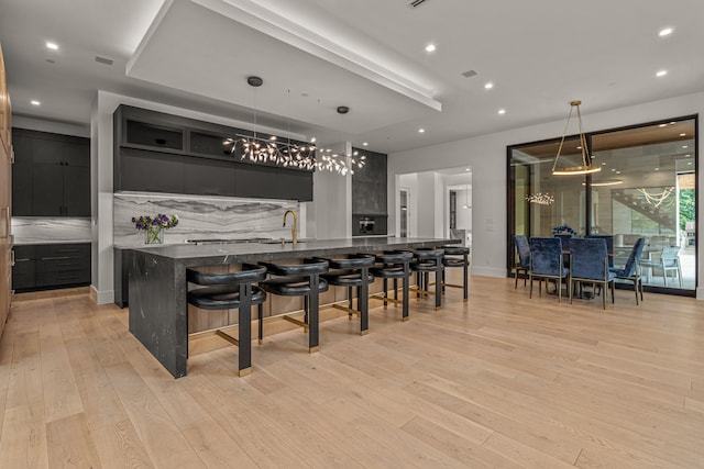 kitchen with decorative backsplash, light wood-type flooring, a kitchen breakfast bar, hanging light fixtures, and a large island with sink